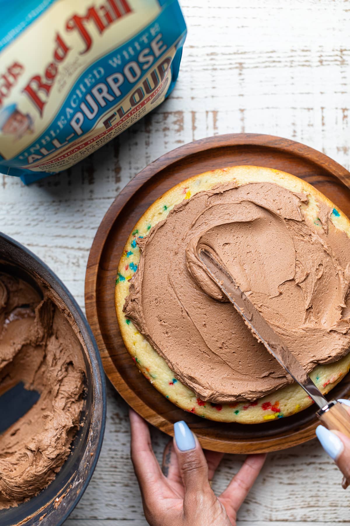 Confetti Chocolate Chip Cake being topped with frosting.