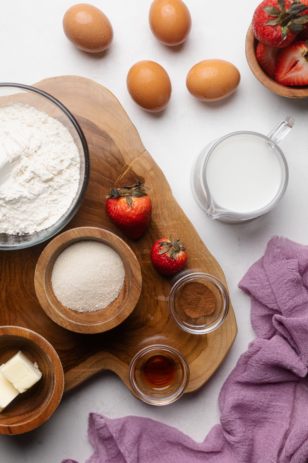 Ingredients on a table and wooden board including butter, sugar, and strawberries.