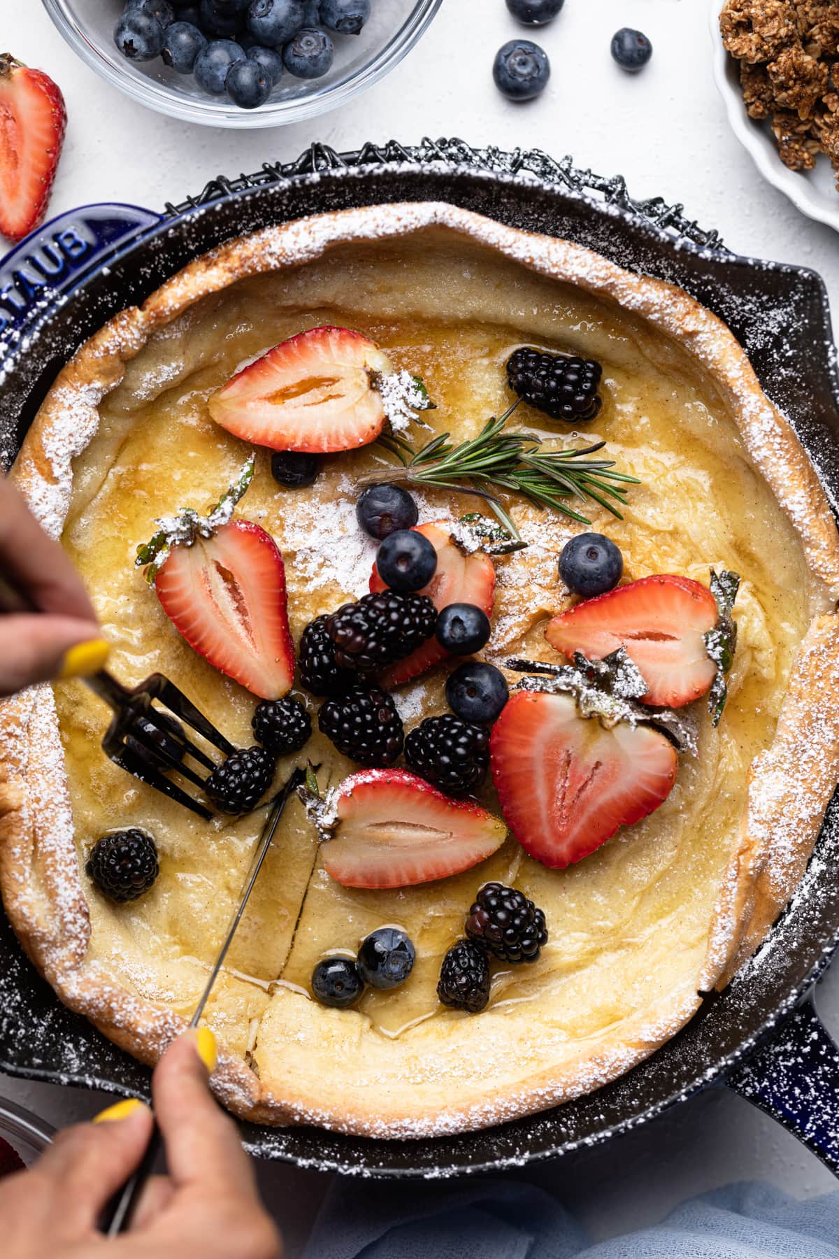 Person using a fork to grab part of a Dutch Baby Pancake with Berries.