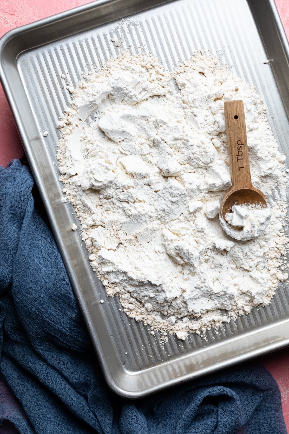 Flour and a measuring spoon on a baking sheet.