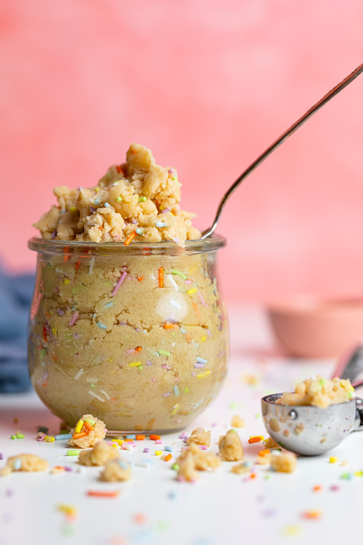 Edible Vegan Funfetti Cookie Dough in a glass and crumbled on a table.