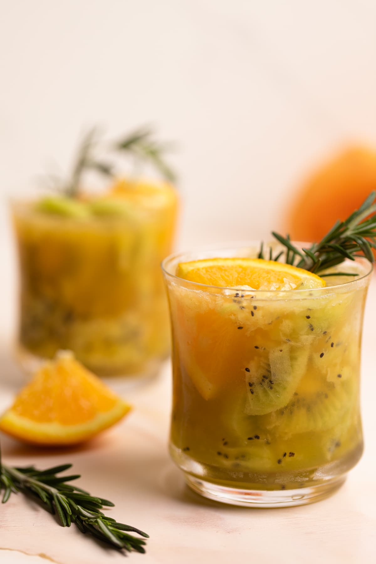 Glasses of Orange Kiwi Ginger Mocktail on a table with orange pieces.