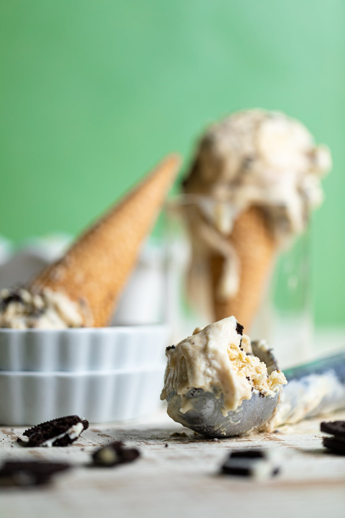 Ice cream in a scoop with ice cream cones in the background and crushed oreo cookies.