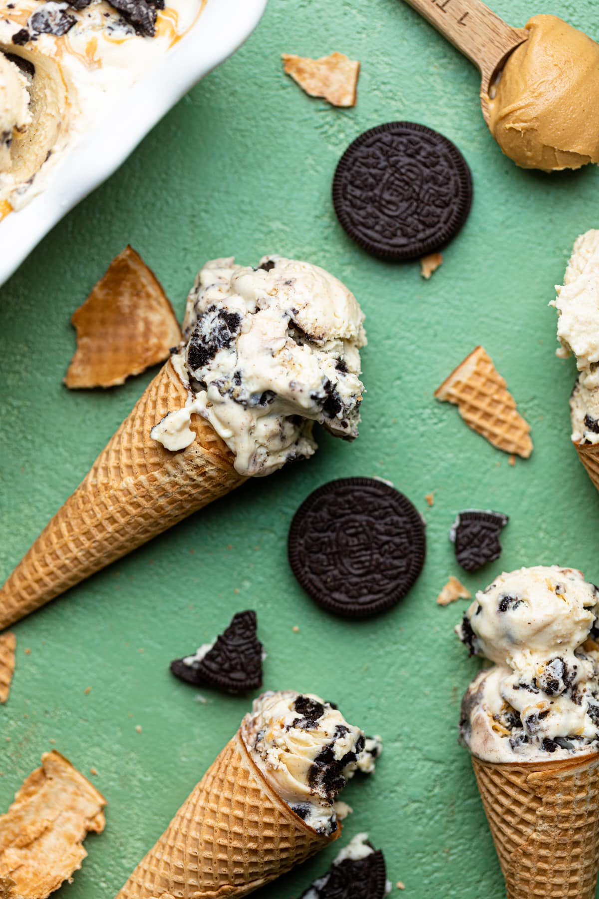 Ice cream on a cone laying on a green table with other ice creams and oreo cookies.