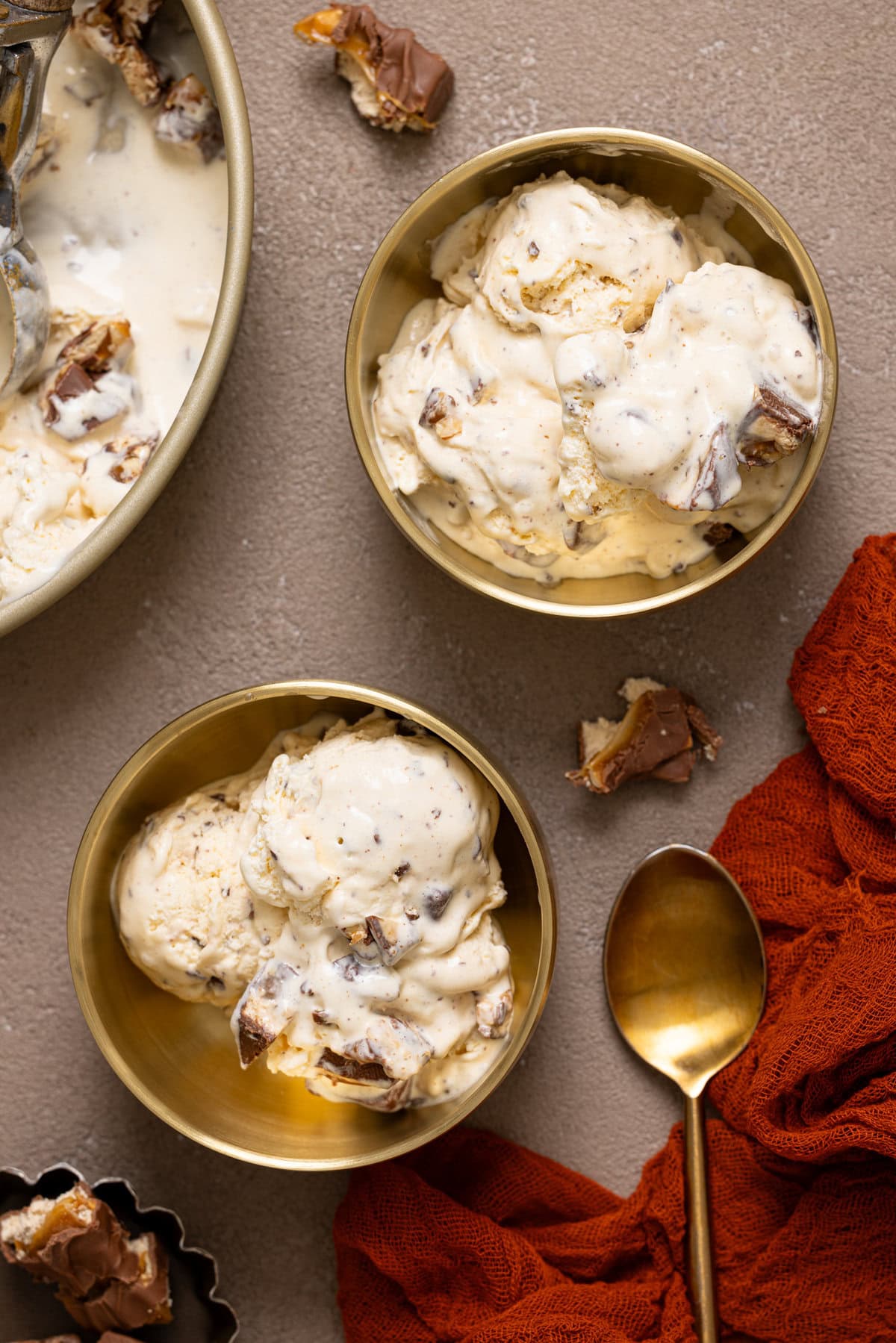 Two gold bowls of ice cream with a spoon and pieces of candy.