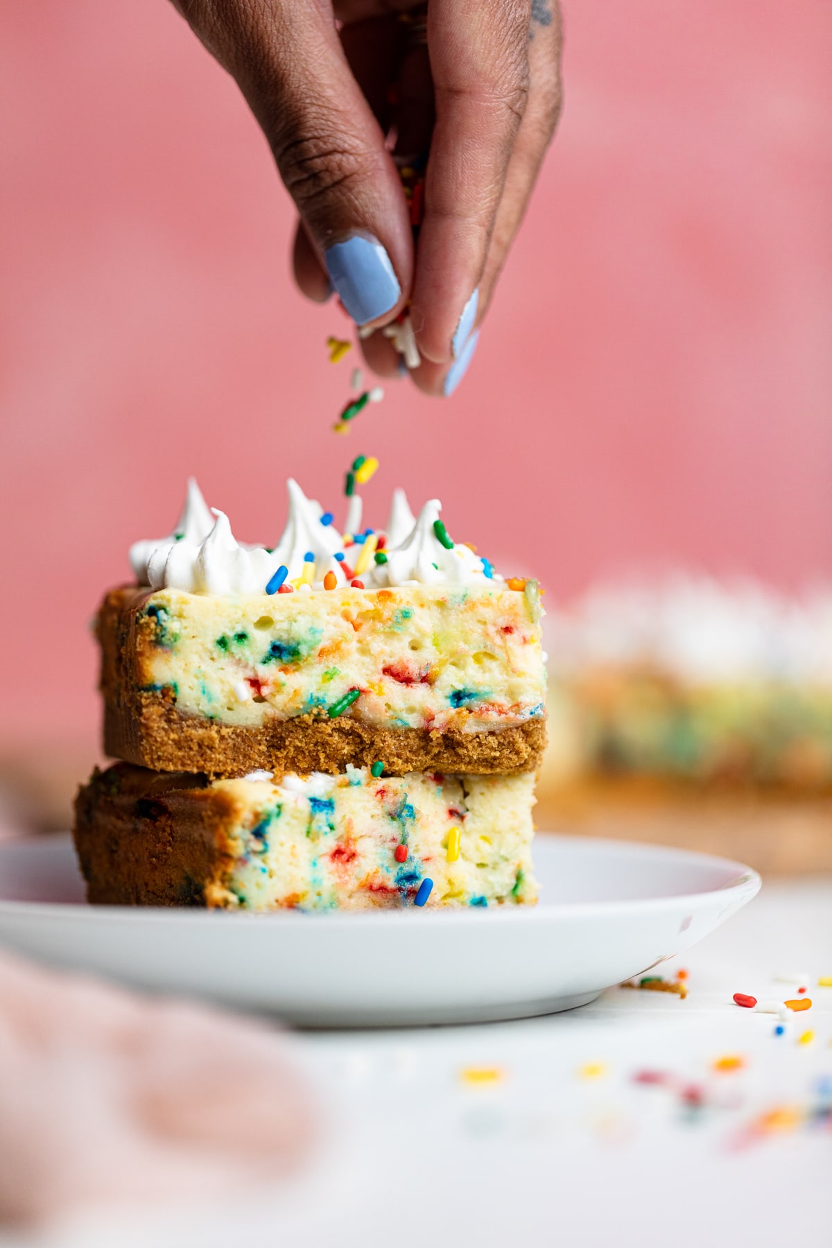 Woman dropping sprinkles onto a stack of Funfetti Cheesecake Bars.