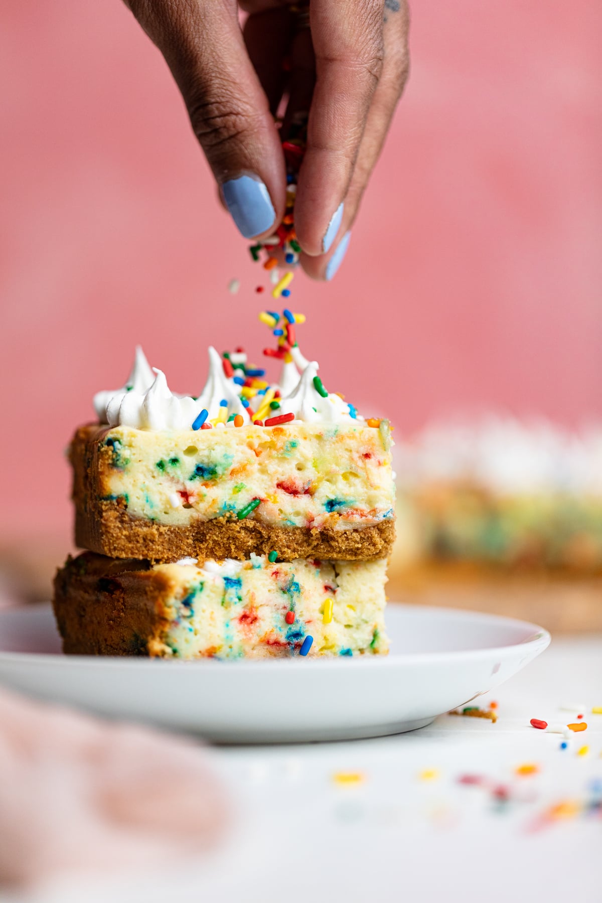 Woman dropping colorful sprinkles onto Funfetti Cheesecake Bars.