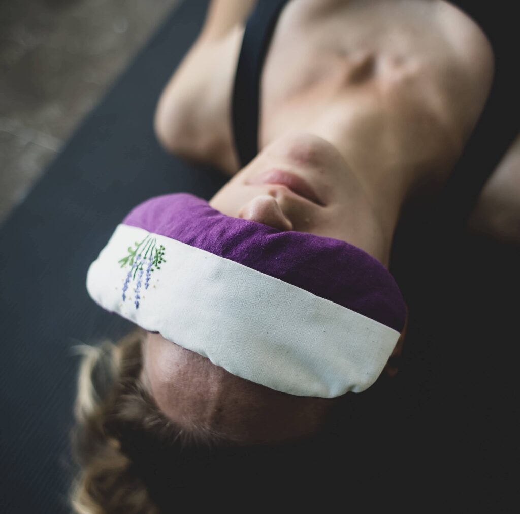 Woman lying down wearing a purple and white eye mask