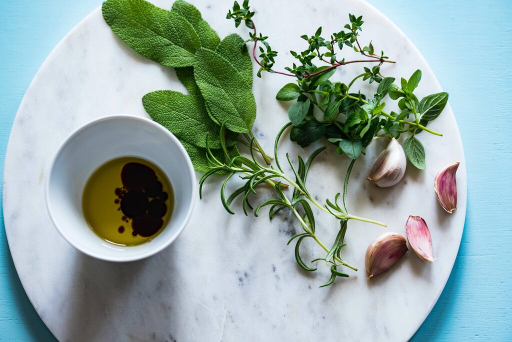 Small bowl of oil next to various herbs.