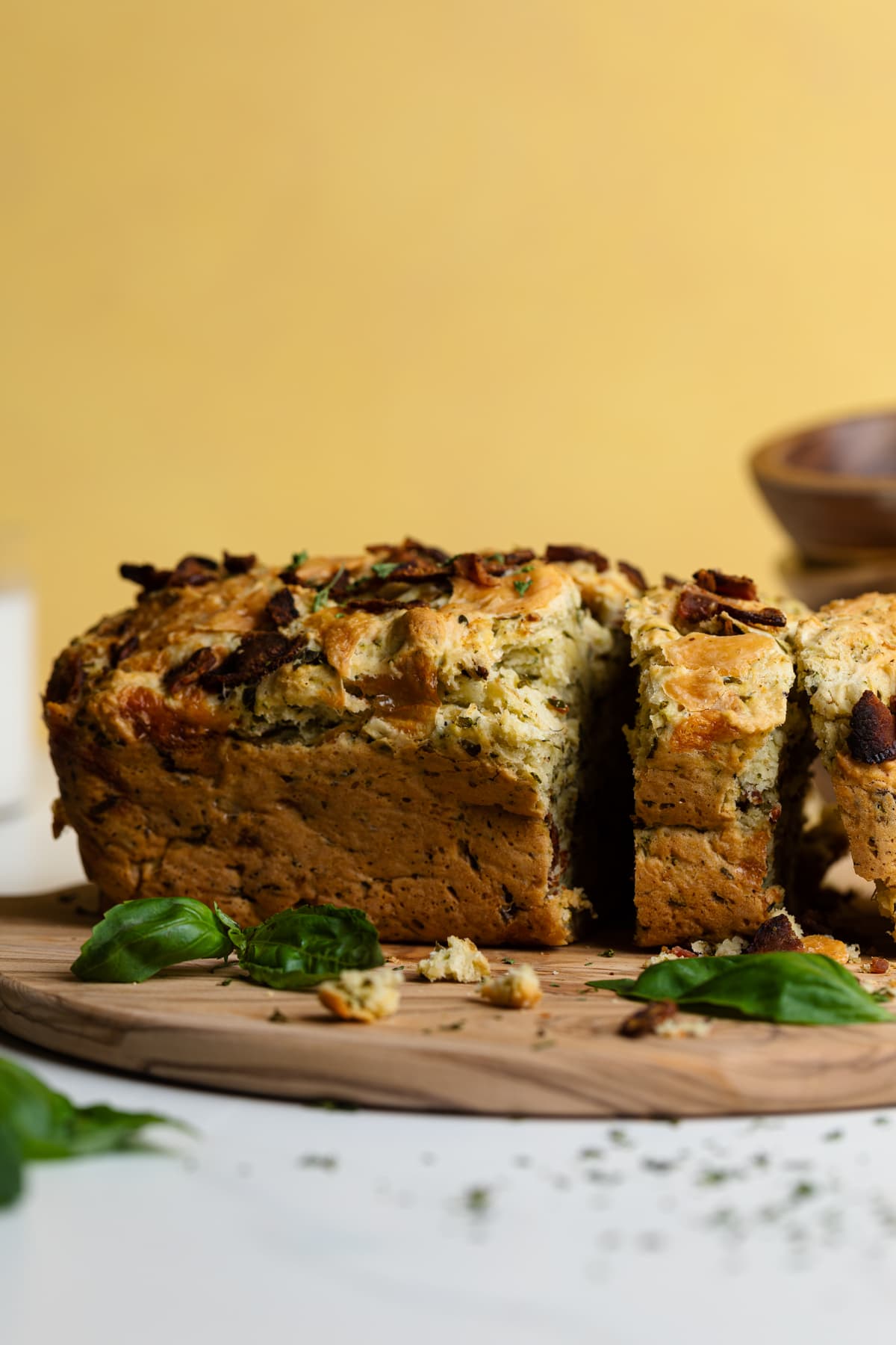 Loaf of Loaded Cheddar Pesto Zucchini Bread with Bacon on a board with herbs.