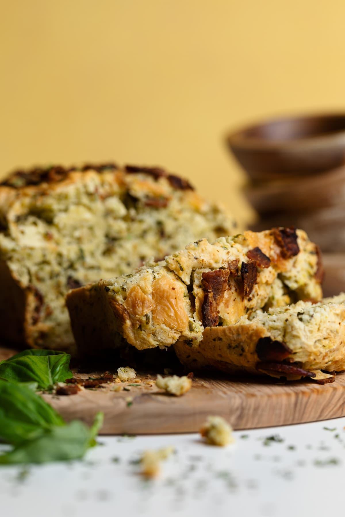 Slices of Loaded Cheddar Pesto Zucchini Bread with Bacon piled on a wooden board.