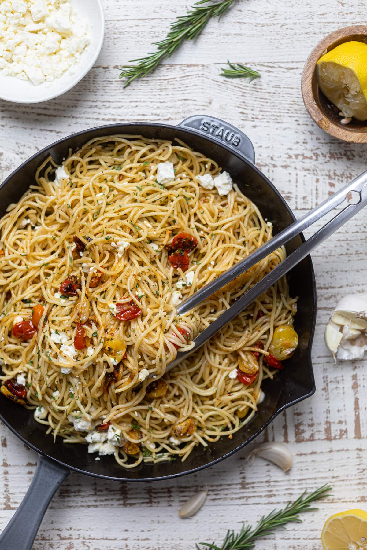 Tongs grabbing Lemon Brown Butter Spaghetti with Roasted Tomatoes and Feta from a skillet