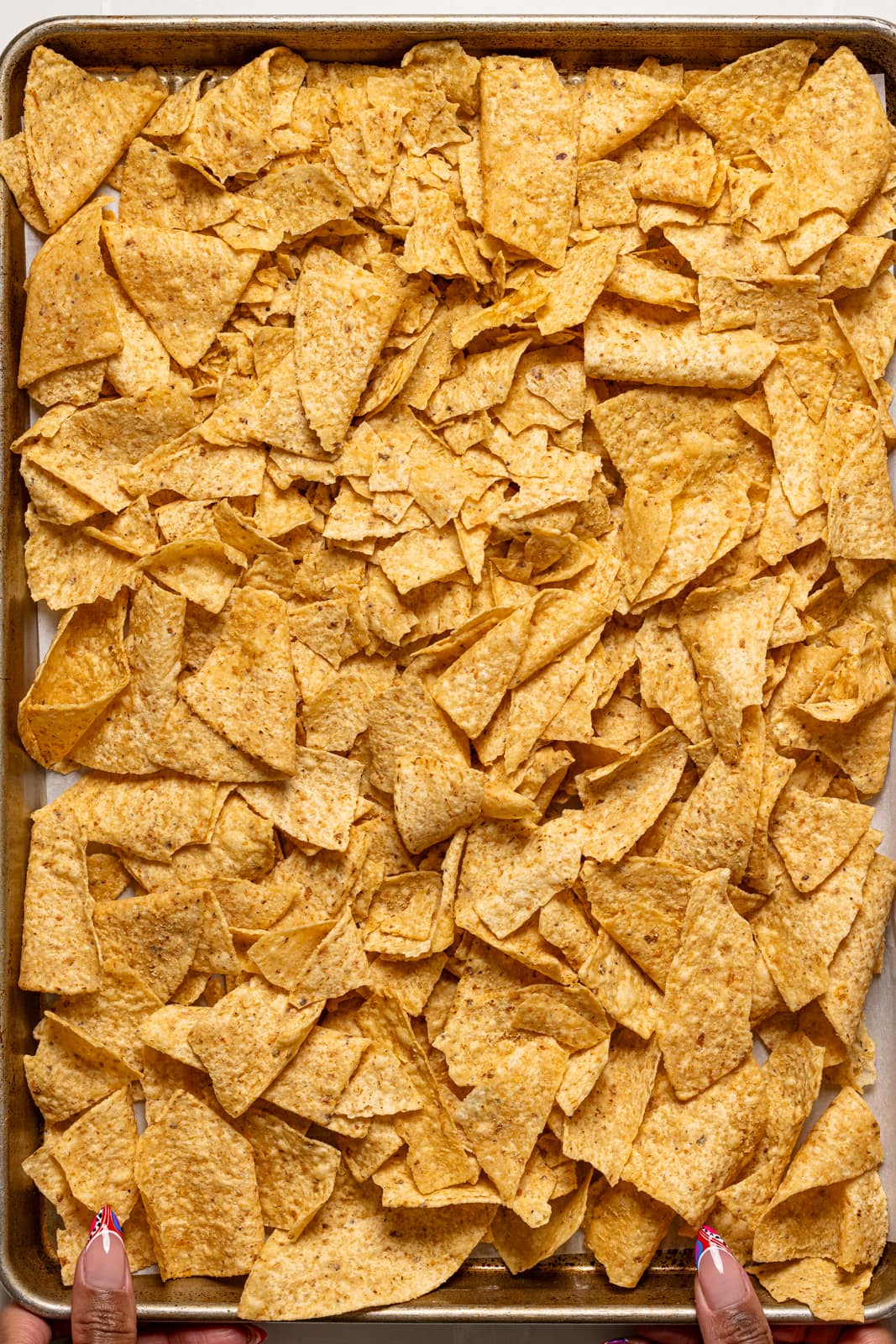 Nachos spread out on a baking sheet.