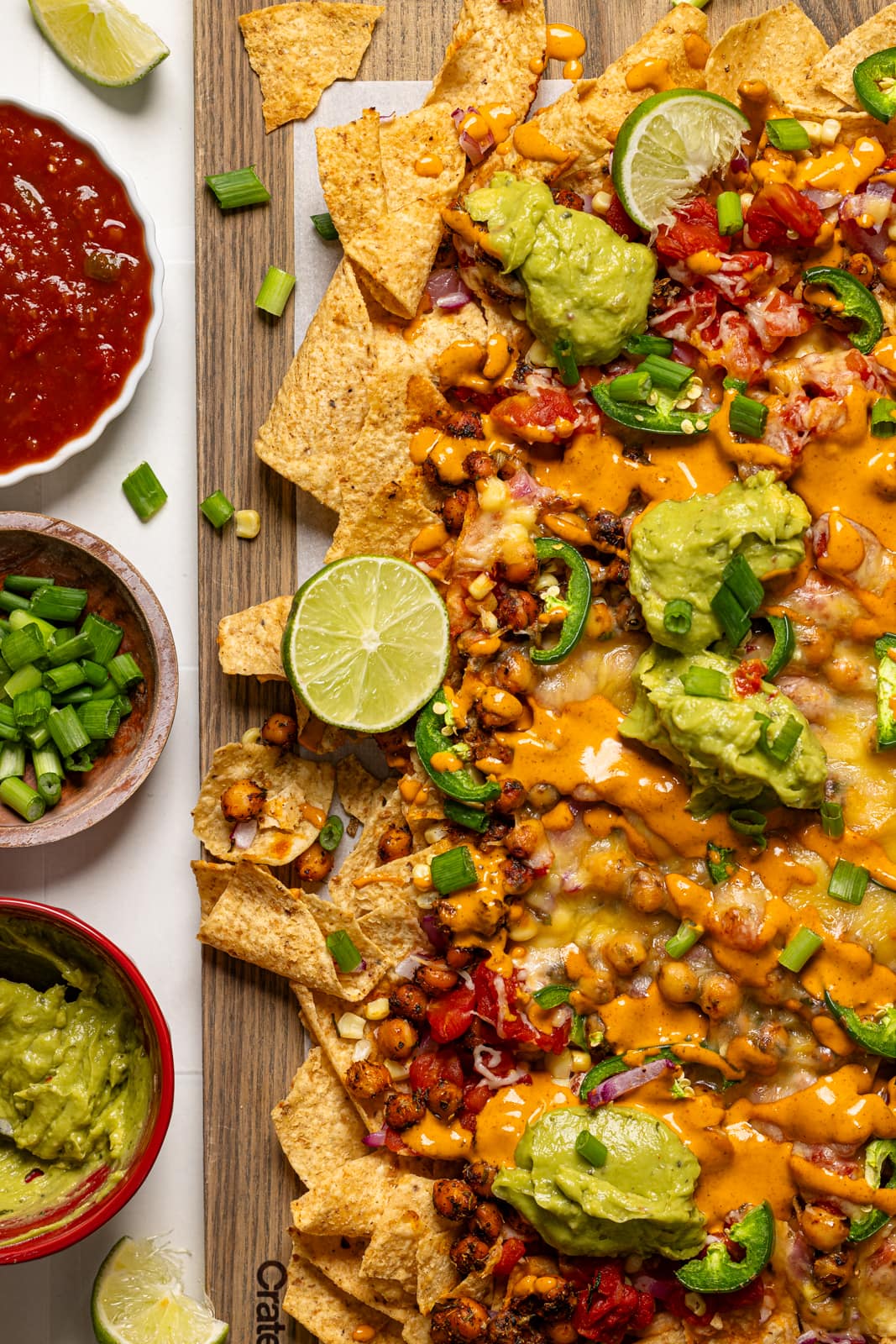 Baked nachos on a wood board with a side of toppings.