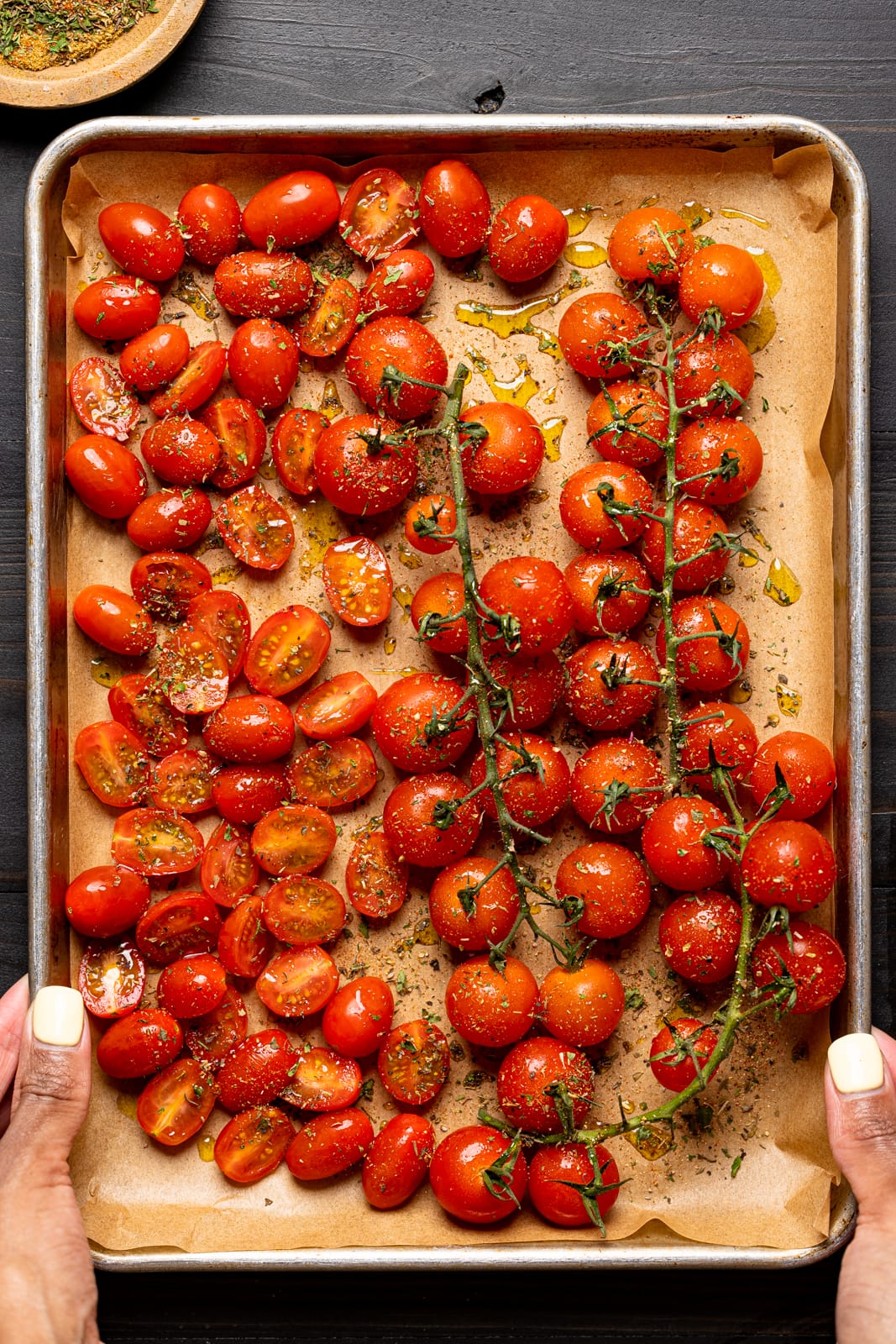 Tomatoes on a baking sheet lined with parchment paper, seasoned and drizzled with olive oil.