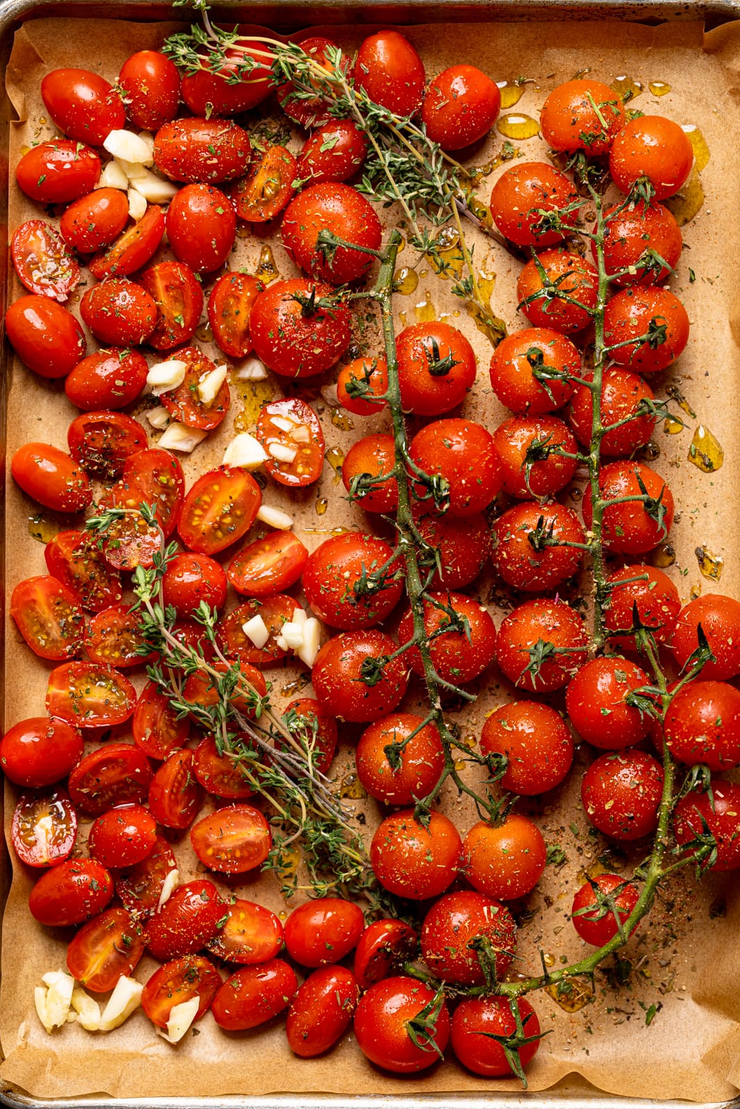 Prepped tomatoes, minced garlic, and herbs on a baking sheet lined with parchment paper. 