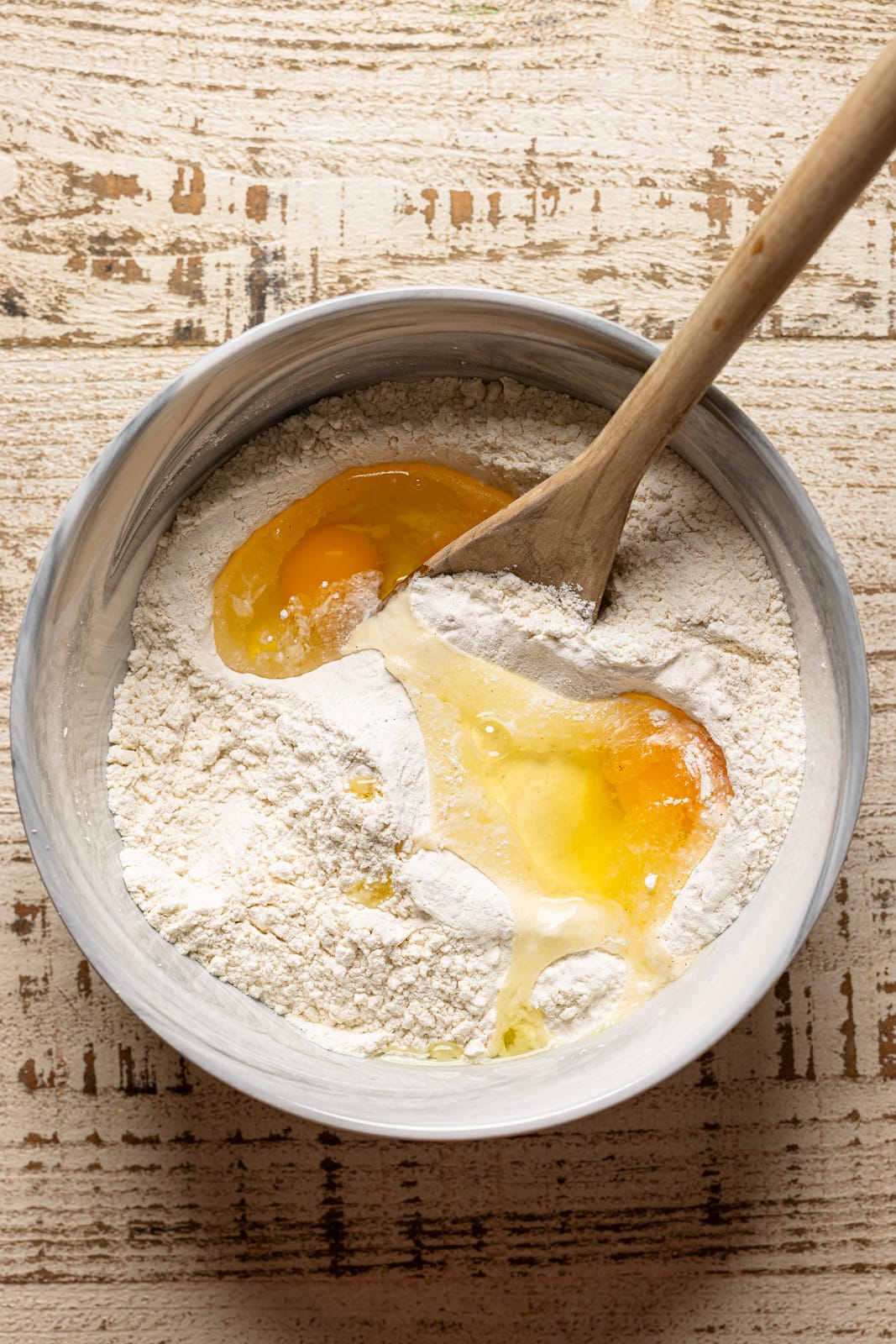 Bowl with batter ingredients and a wooden spoon.