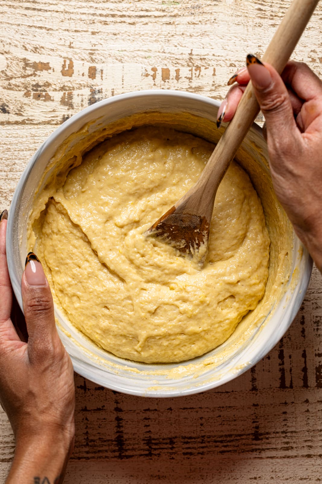 Cake batter in a bowl being held with a wooden spoon.