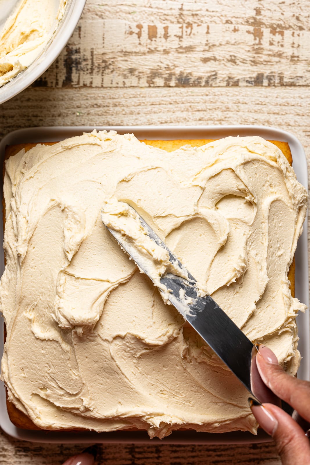 Frosting on a cake being spread with a spatula. 