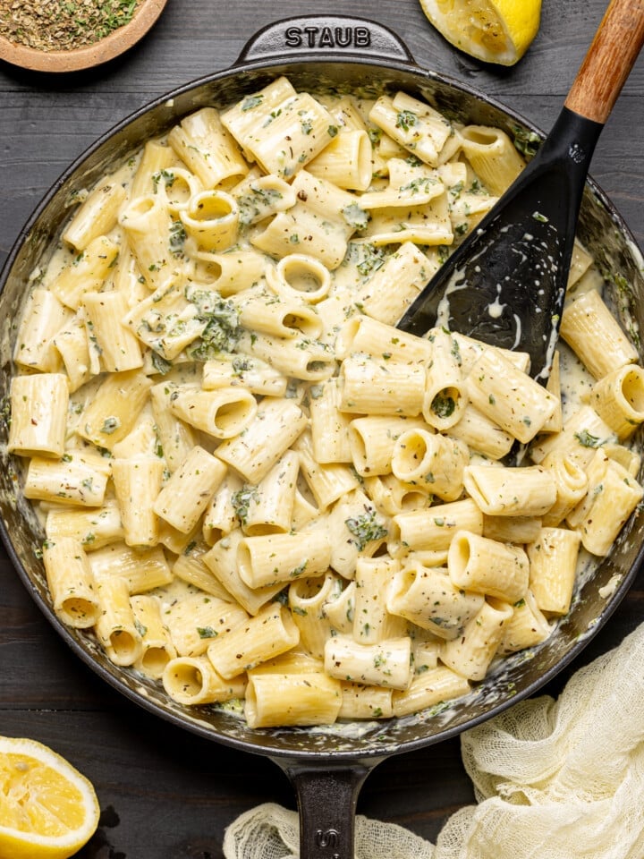 Creamy pasta in a black skillet with a spoon and lemons.