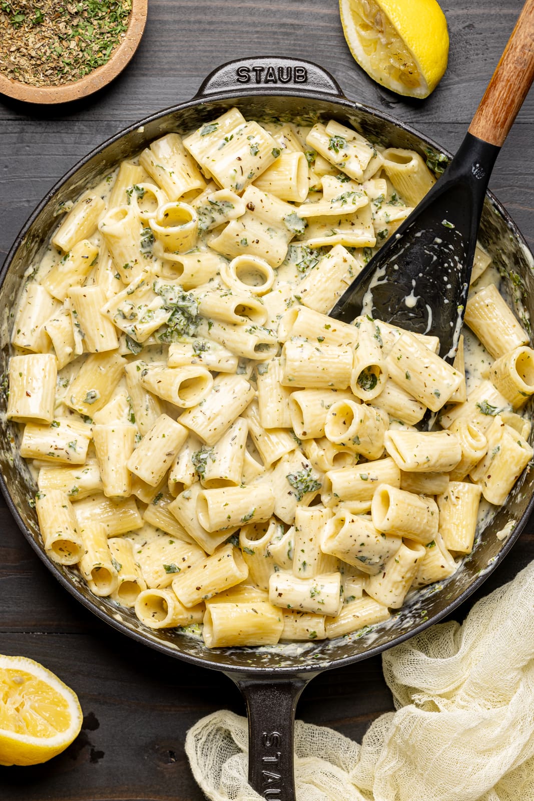 Creamy pasta in a black skillet with a spoon and lemons. 