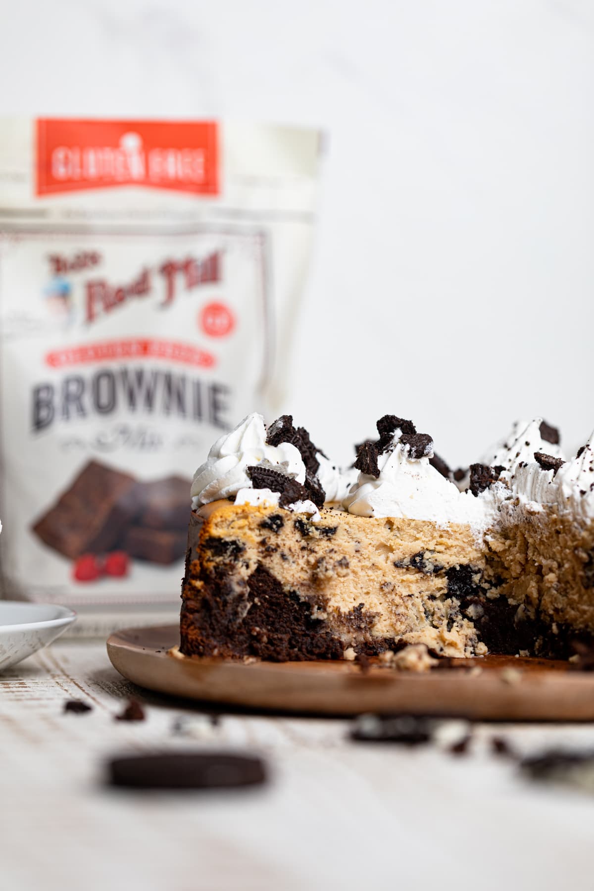 Gluten-Free Peanut Butter Cookies N\' Cream Brownie Cheesecake missing a piece in front of a bag of Bob\'s Red Mill gluten free brownie mix