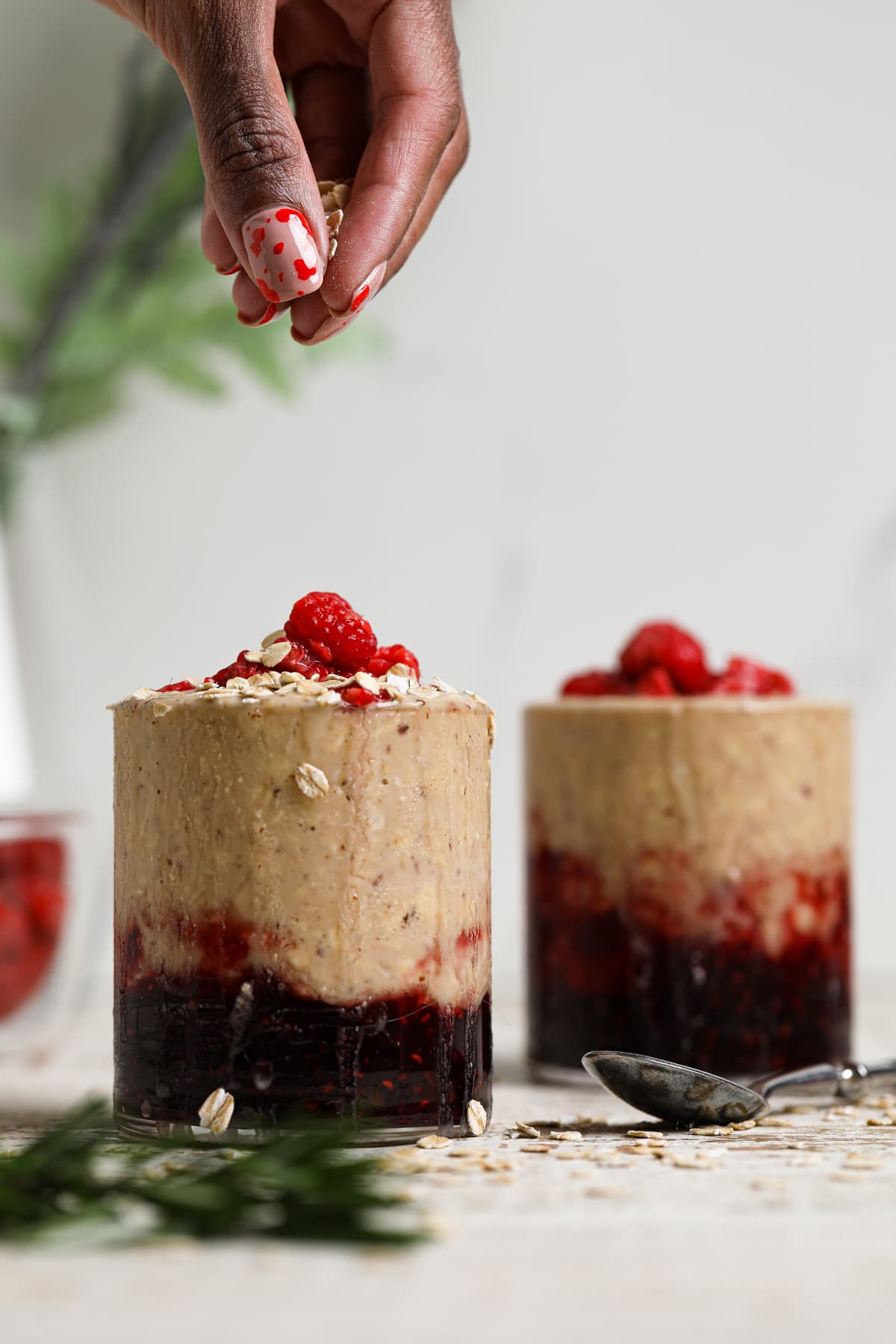 Woman sprinkling oats onto a glass of Protein Peanut Butter and Jelly Overnight Oats.