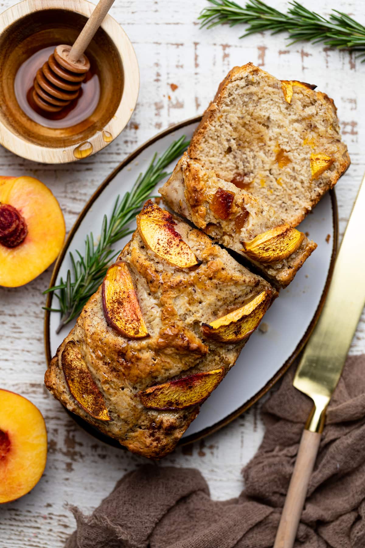 Partially sliced loaf of Cinnamon Maple Peach Bread on a platter set on a white table