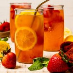 Three tall glasses of lemonade on a white wood table with strawberries and lemons.