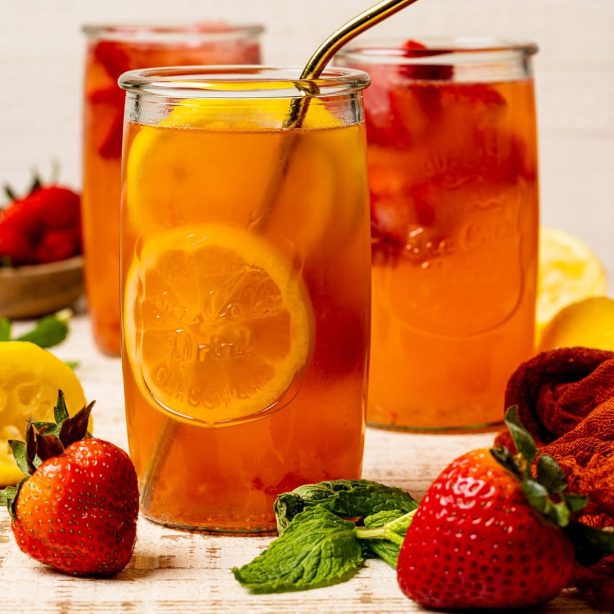 Three tall glasses of lemonade on a white wood table with strawberries and lemons.