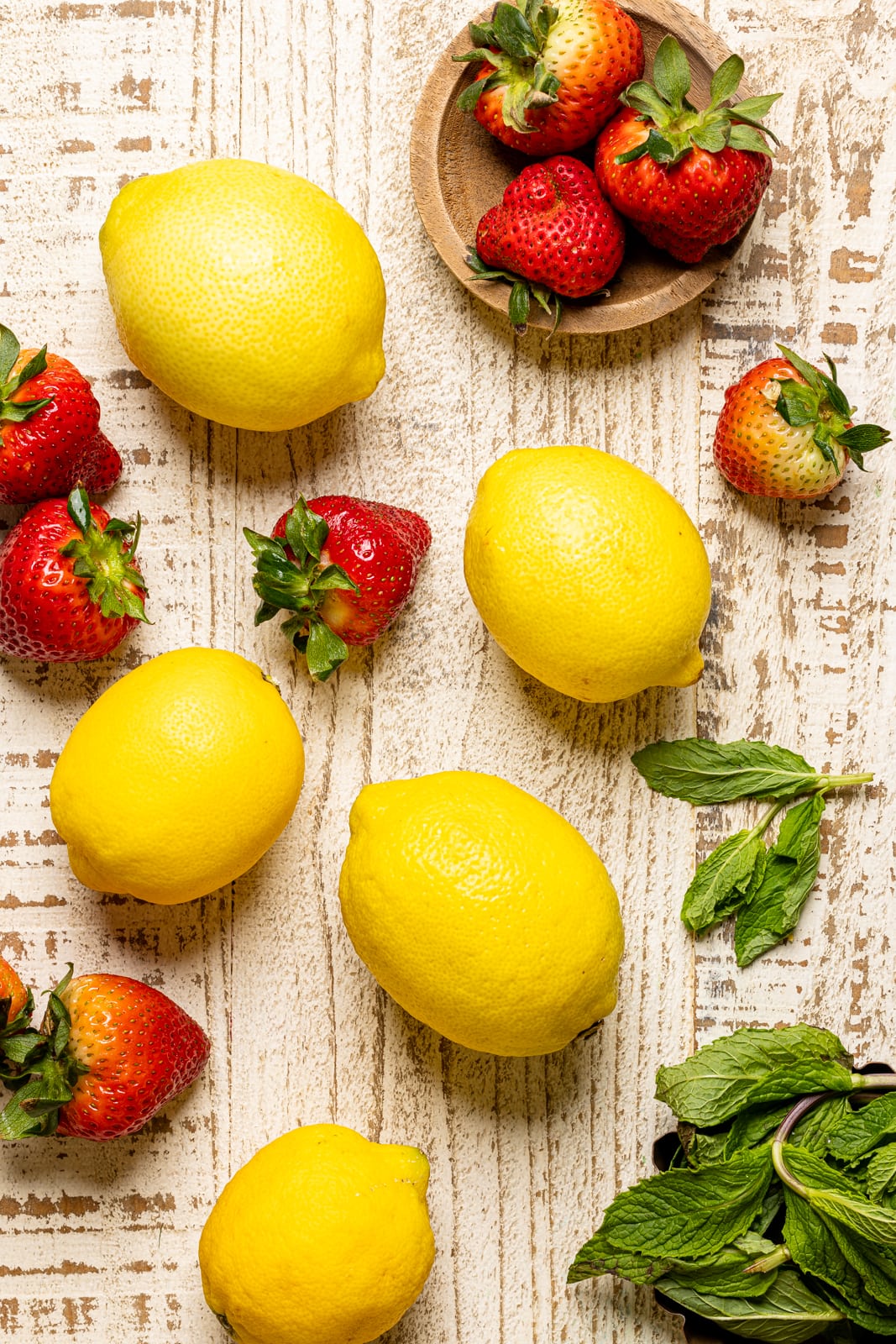 Strawberries and lemons on a white wood table with fresh mint leaves.