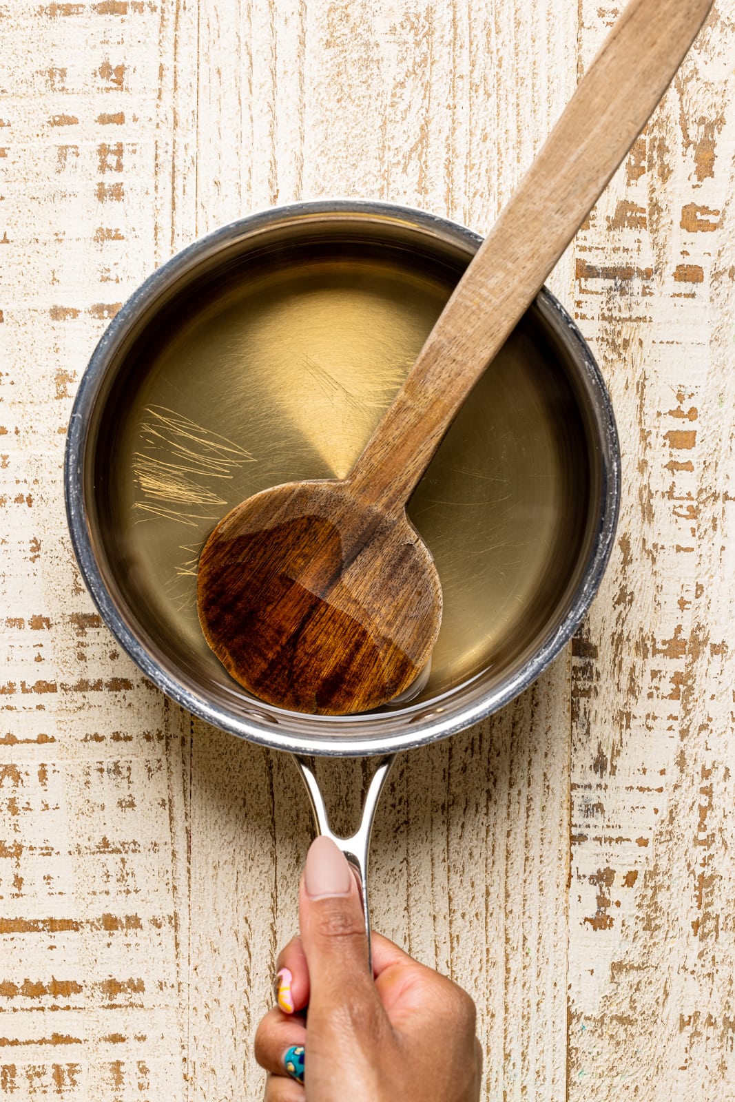 Simple syrup in a saucepan with a wood spoon on a white wood table.