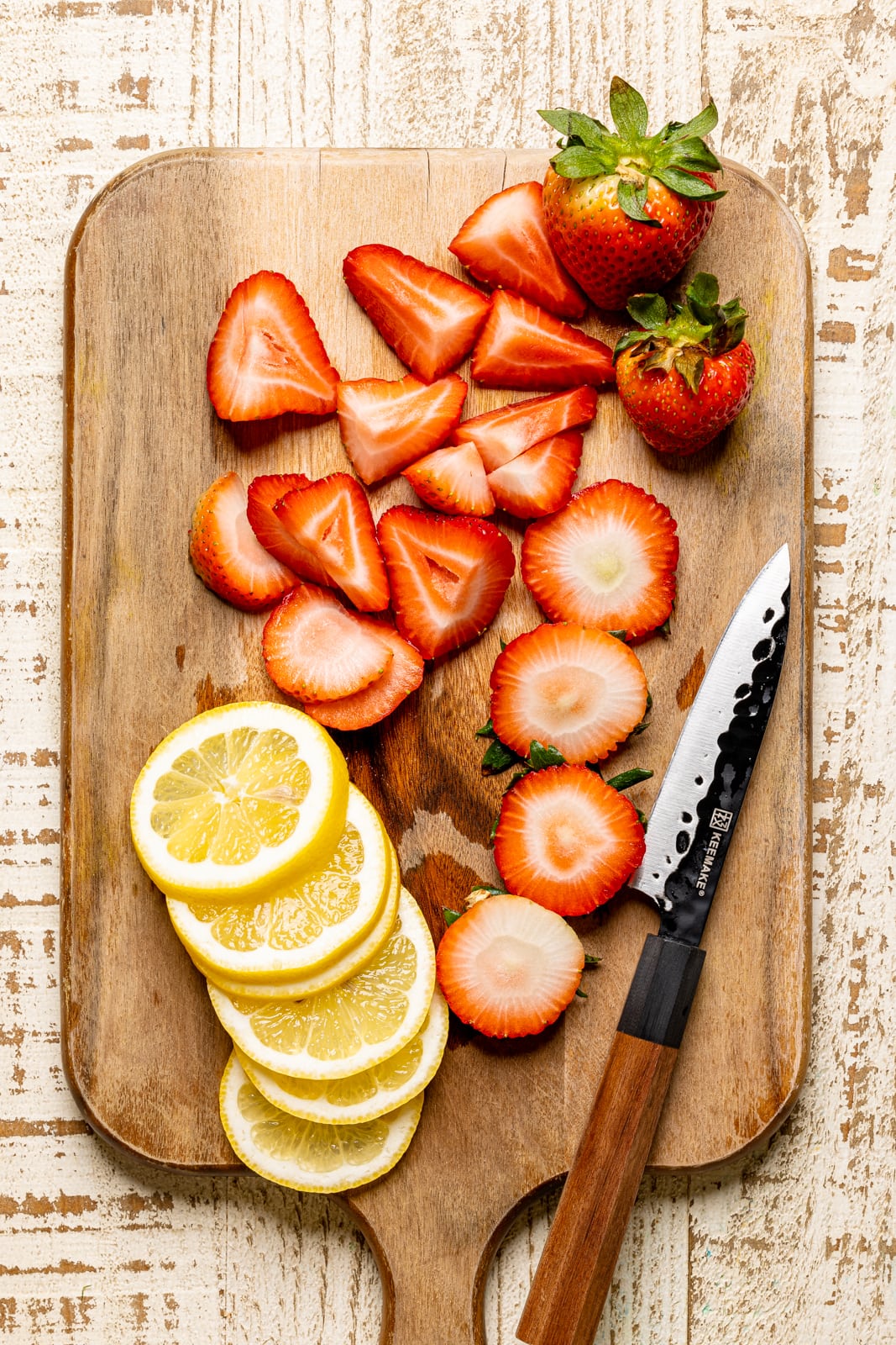 Sliced strawberries and lemons on a cutting board with a knife.