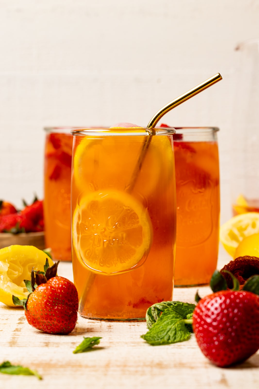 Three tall glasses of lemonade on a white wood table with strawberries and lemons.