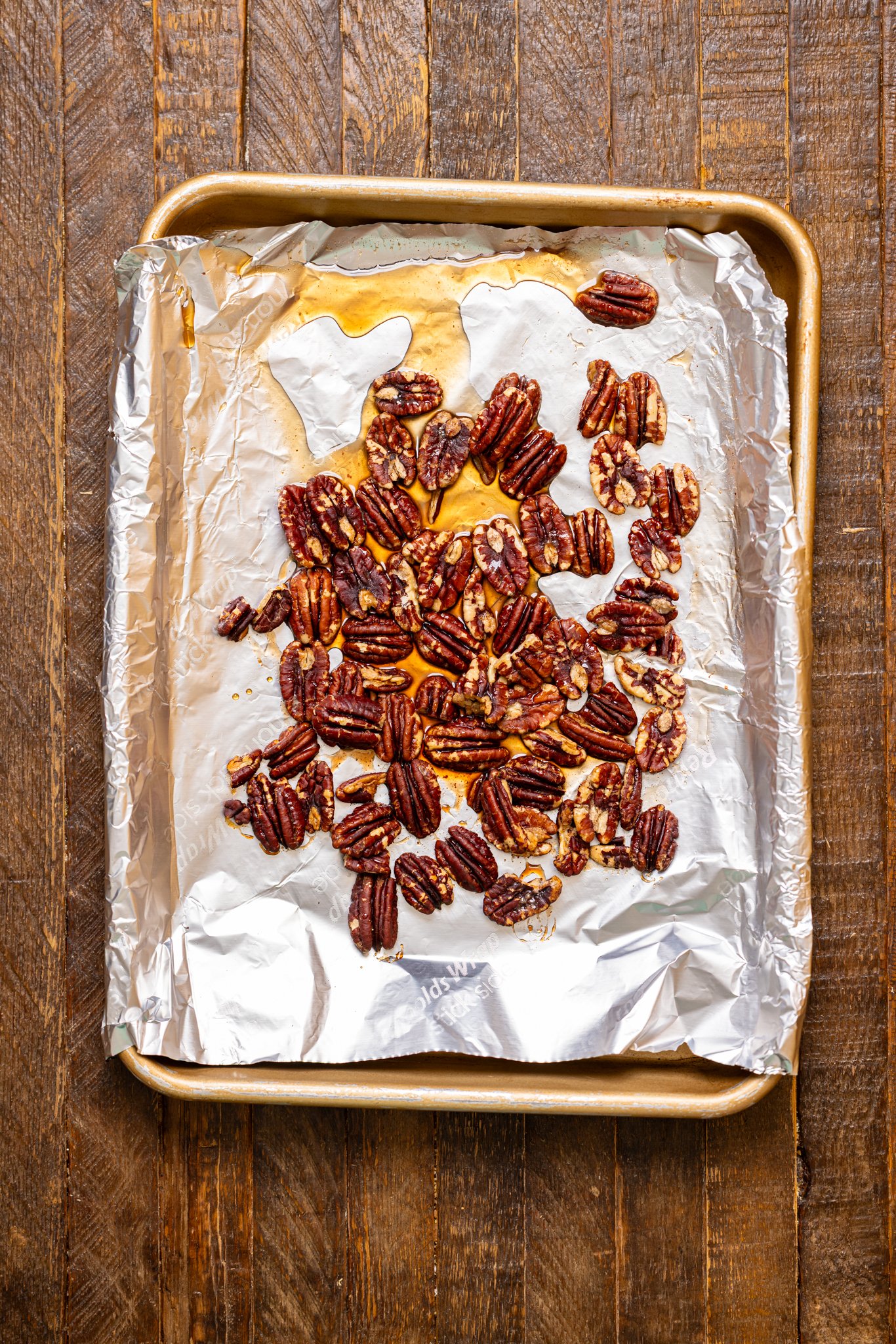 Candied pecans on a baking sheet with foil paper.
