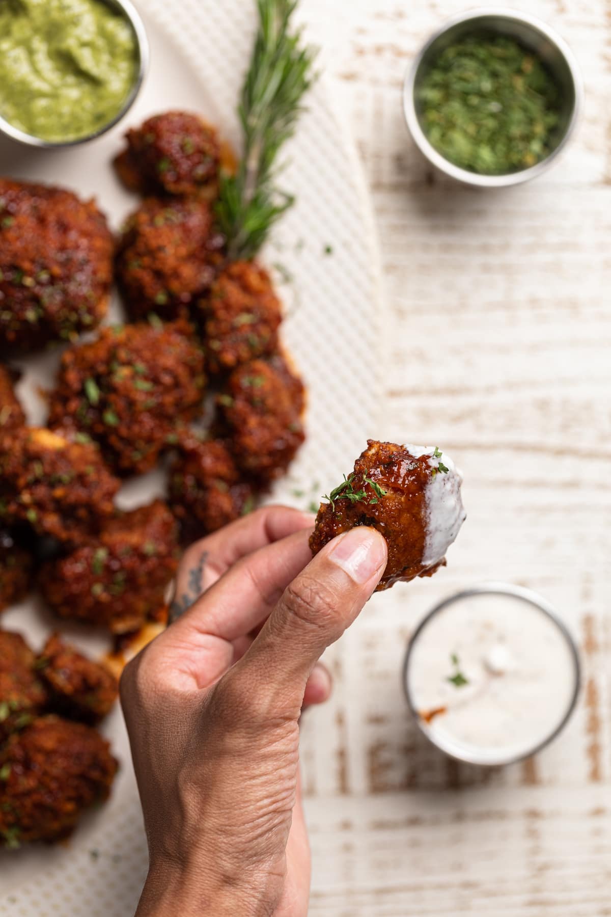 Hand holding a barbeque Cauliflower Wing that has been dipped