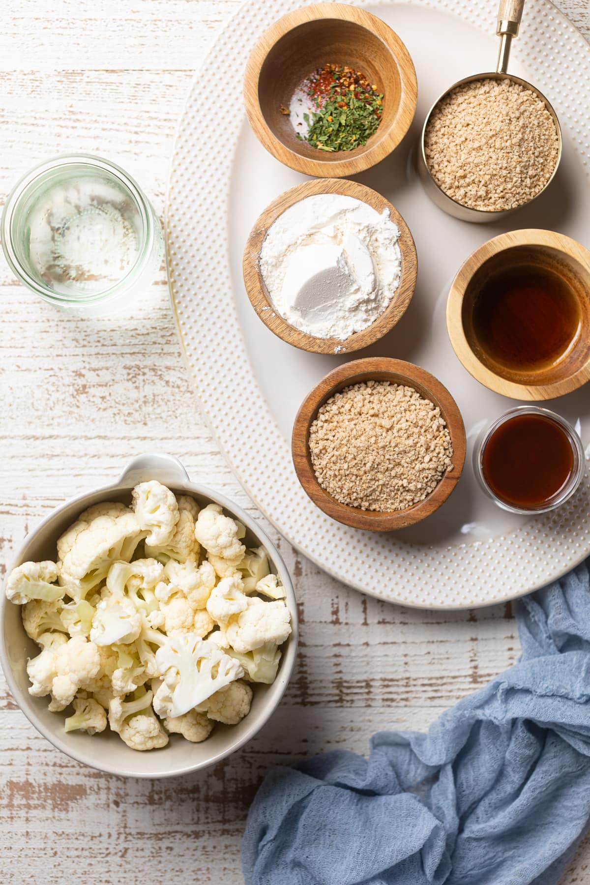 Bowl of chopped cauliflower next to a platter with ingredients like gluten-free flour and honey
