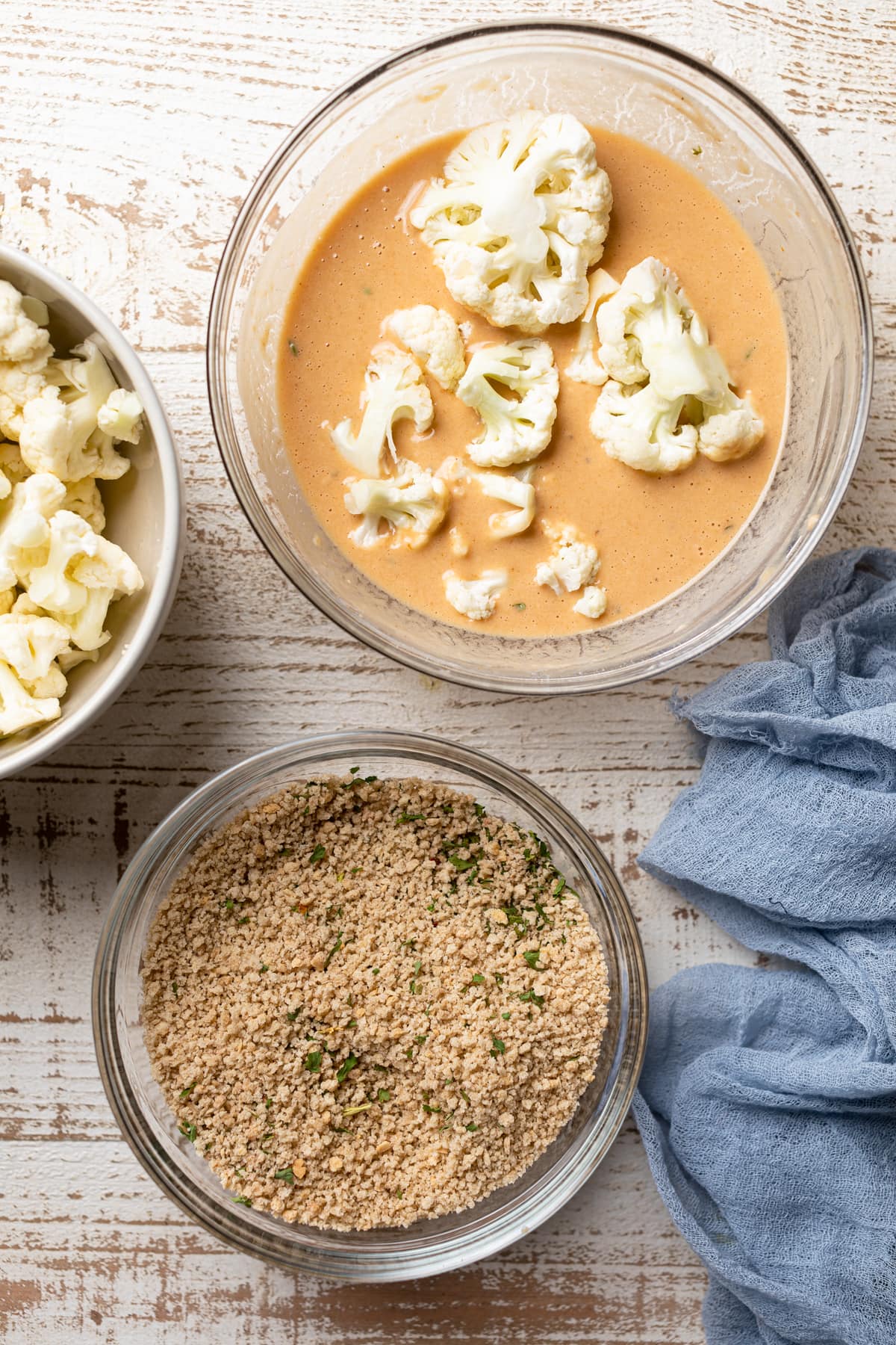 Chopped cauliflower sitting in a bowl of batter next to a bowl of bread crumbs