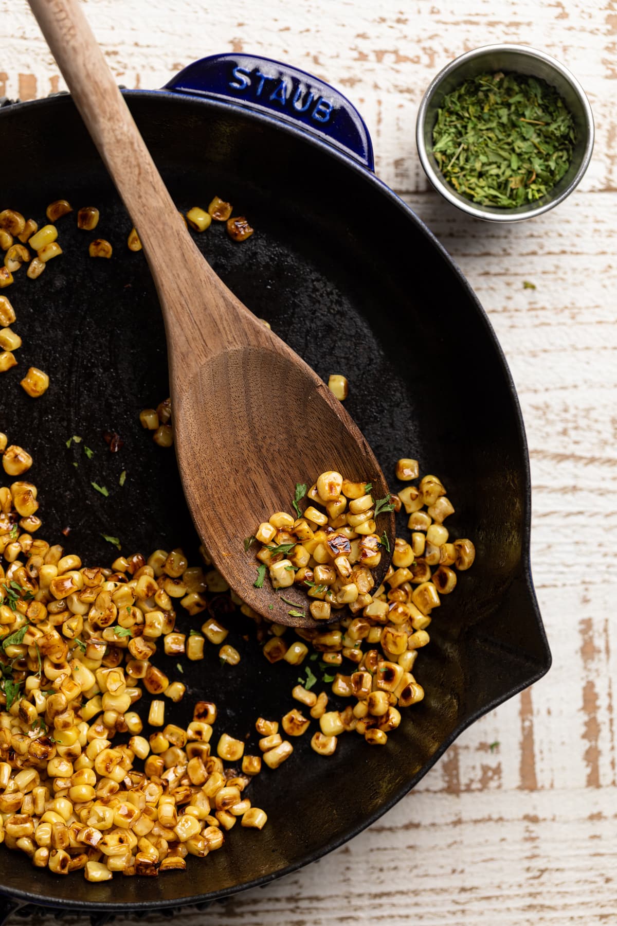 Wooden spoon scooping sauteed corn from a skillet