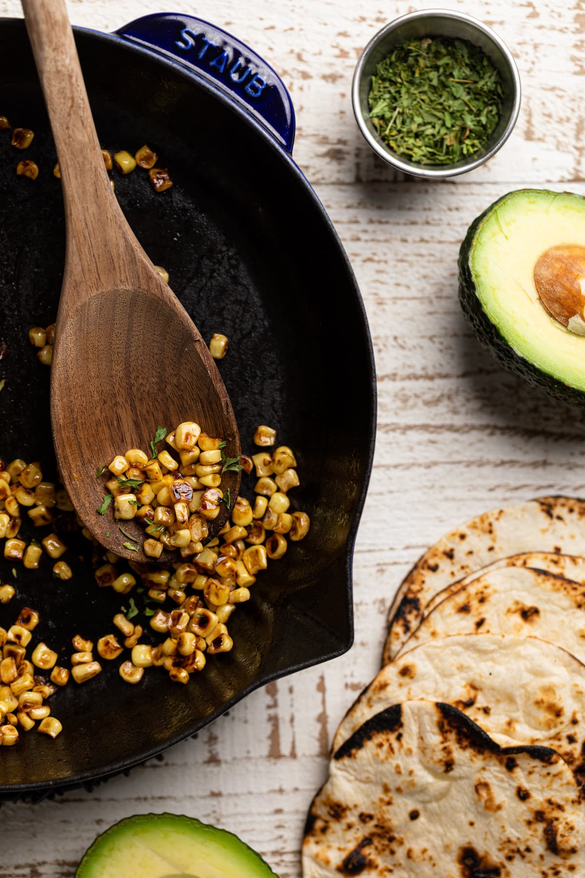 Wooden spoon scooping sauteed corn from a skillet