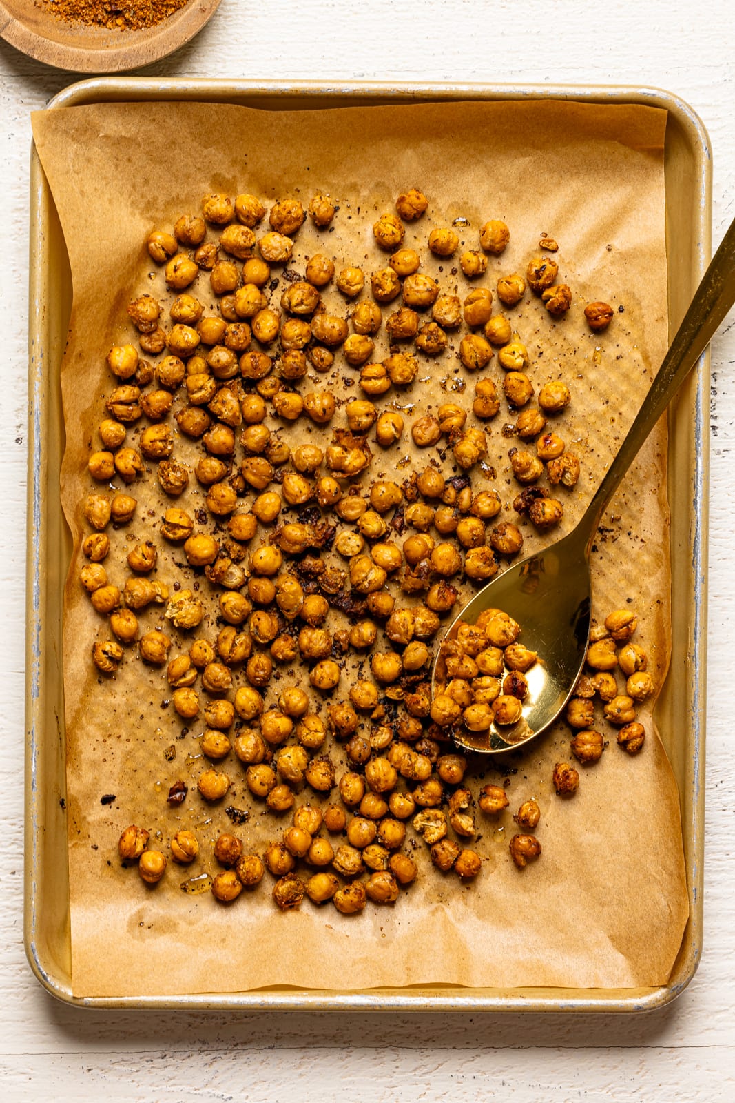 Roasted chickpeas on a baking sheet with parchment paper and a spoon.