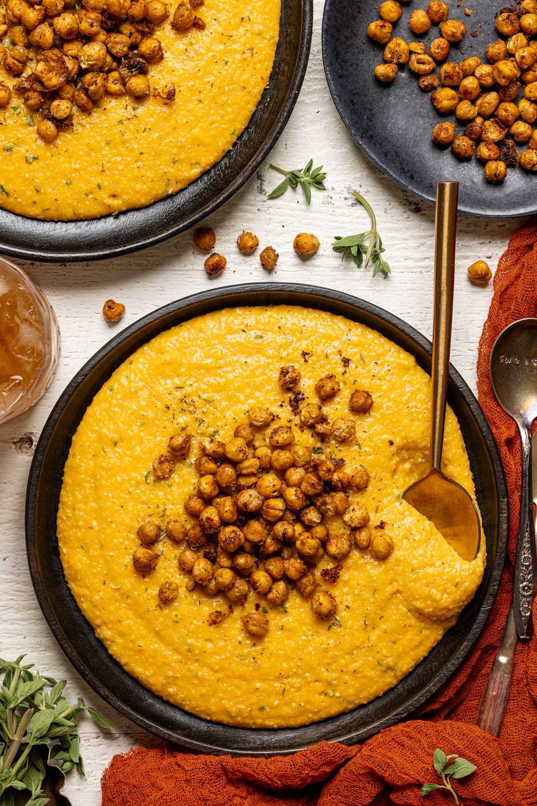 Spoon in a plate of chickpeas and grits with a side of juice and chickpeas on a white wood table.