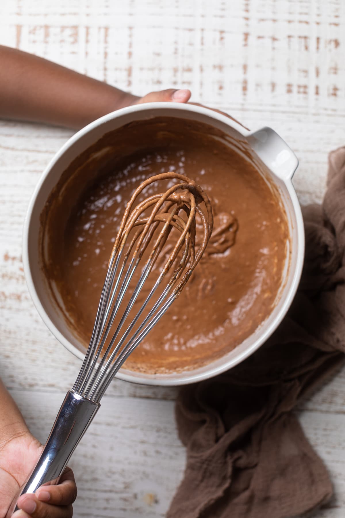 Chocolate glaze on a whisk above a bowl of chocolate glaze