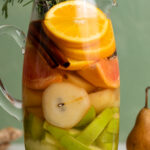 Citrus Ginger Pear Detox Infused Water in a glass pitcher next to fruit.