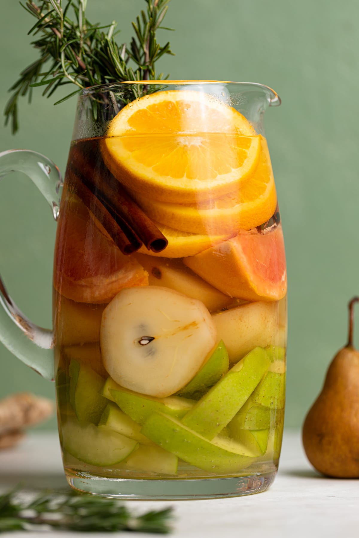 Citrus Ginger Pear Detox Infused Water in a glass pitcher next to fruit.