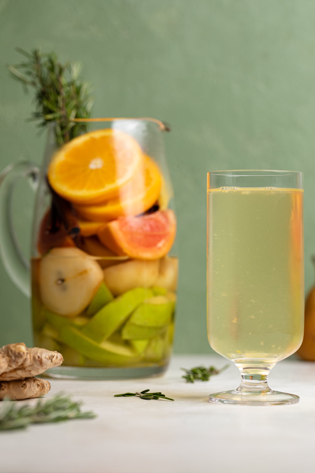 Tall glass of Citrus Ginger Pear Detox Infused Water next to a pitcher with fruit.