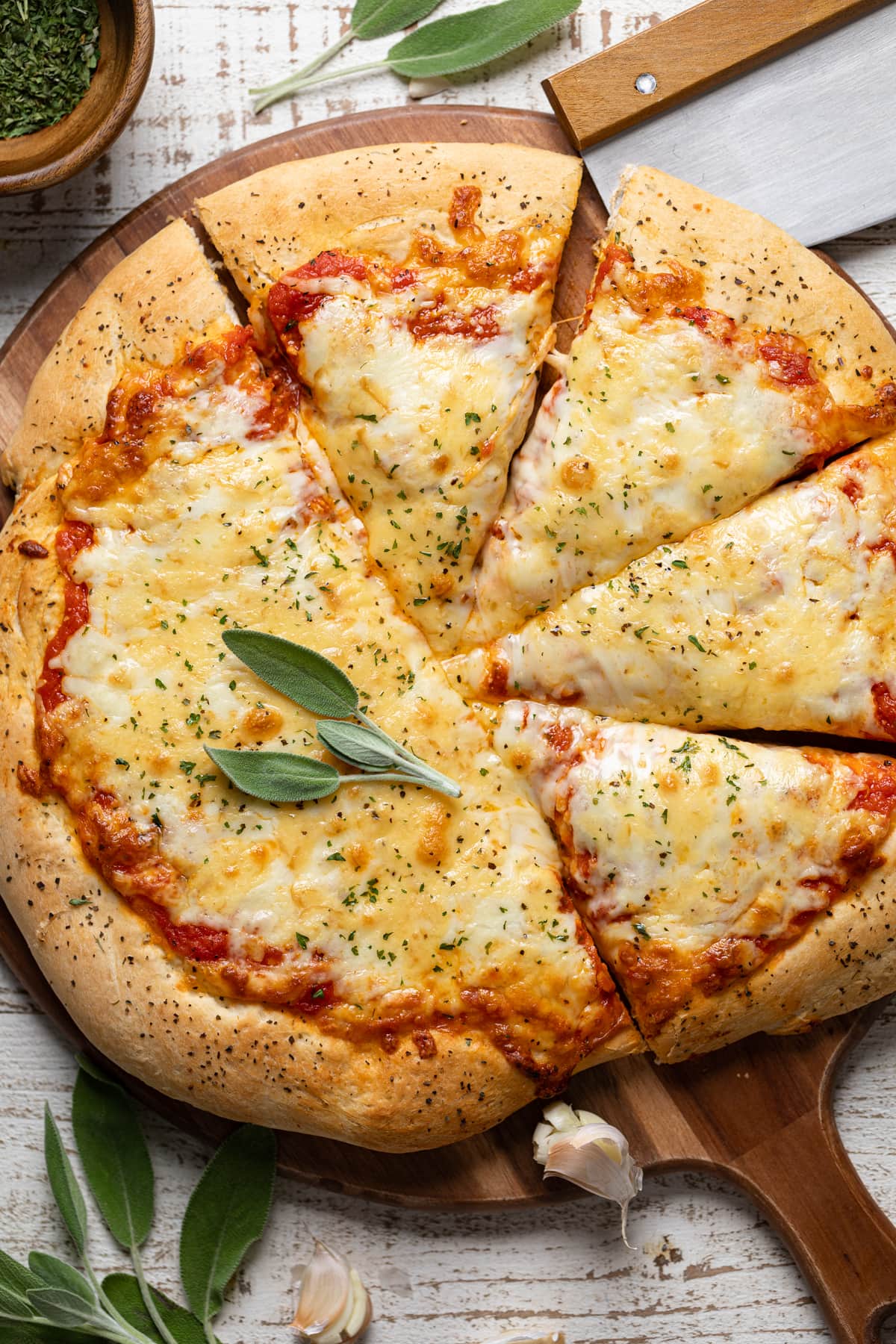 Half-sliced Garlic Herb Cheese Pizza on a wooden board set on a white table