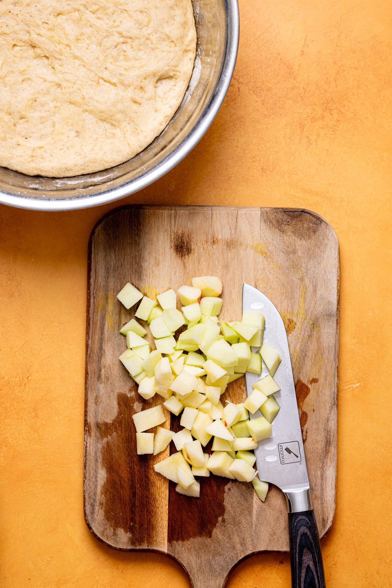 Image of cinnamon roll dough in a bowl and diced apples on cutting board with a knife.