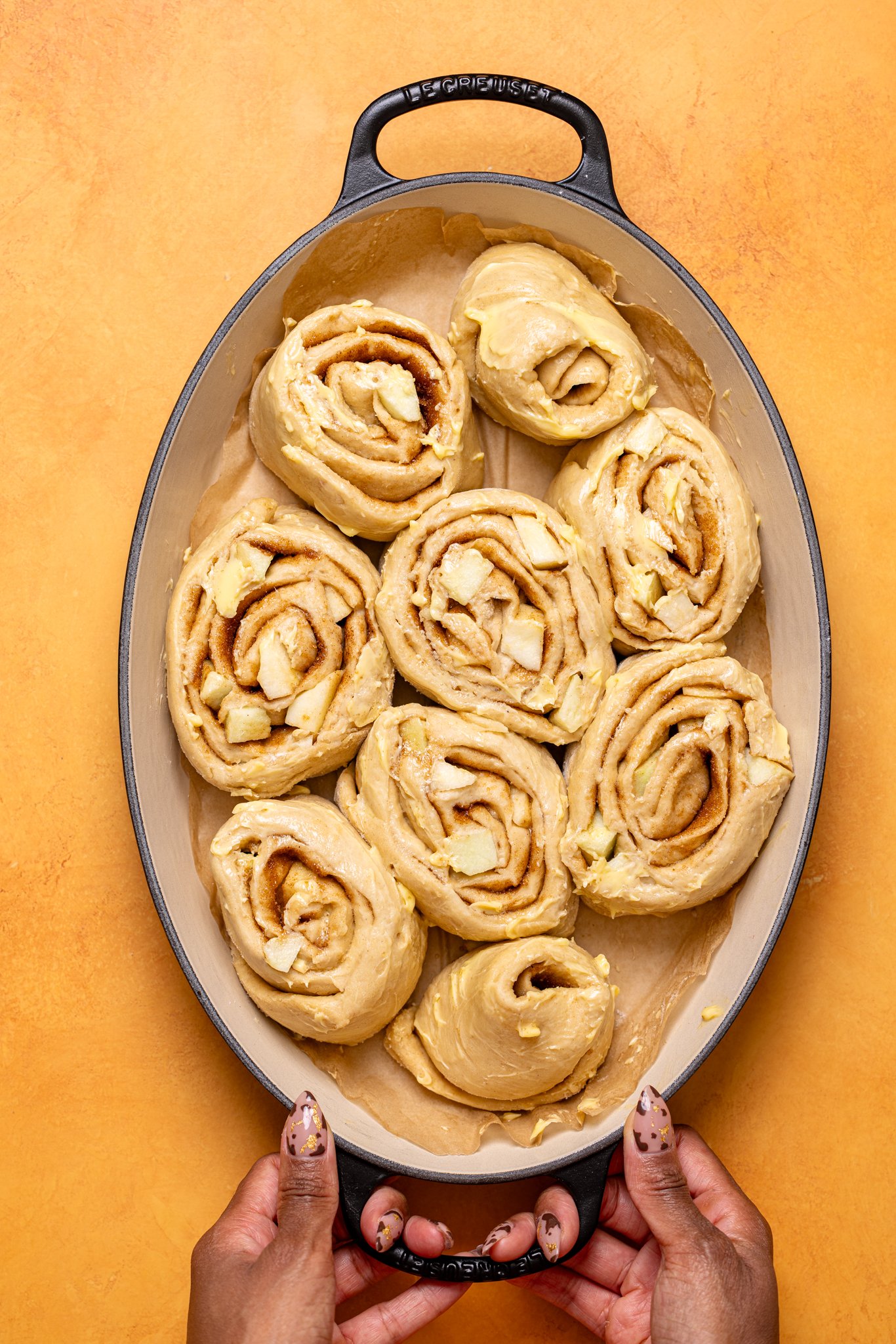 Prepared cinnamon rolls in a baking dish being held by woman hands.