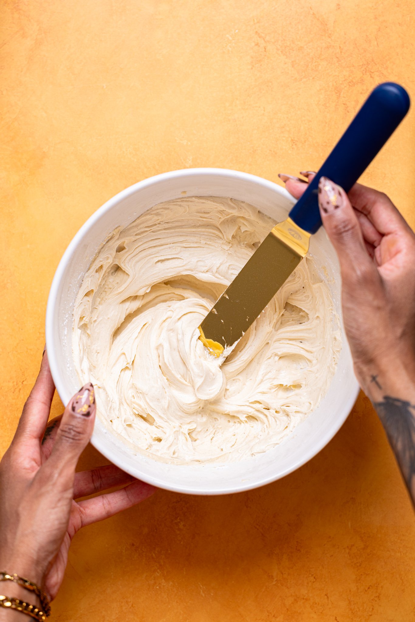 Frosting being stirred together in a bowl with woman hands.